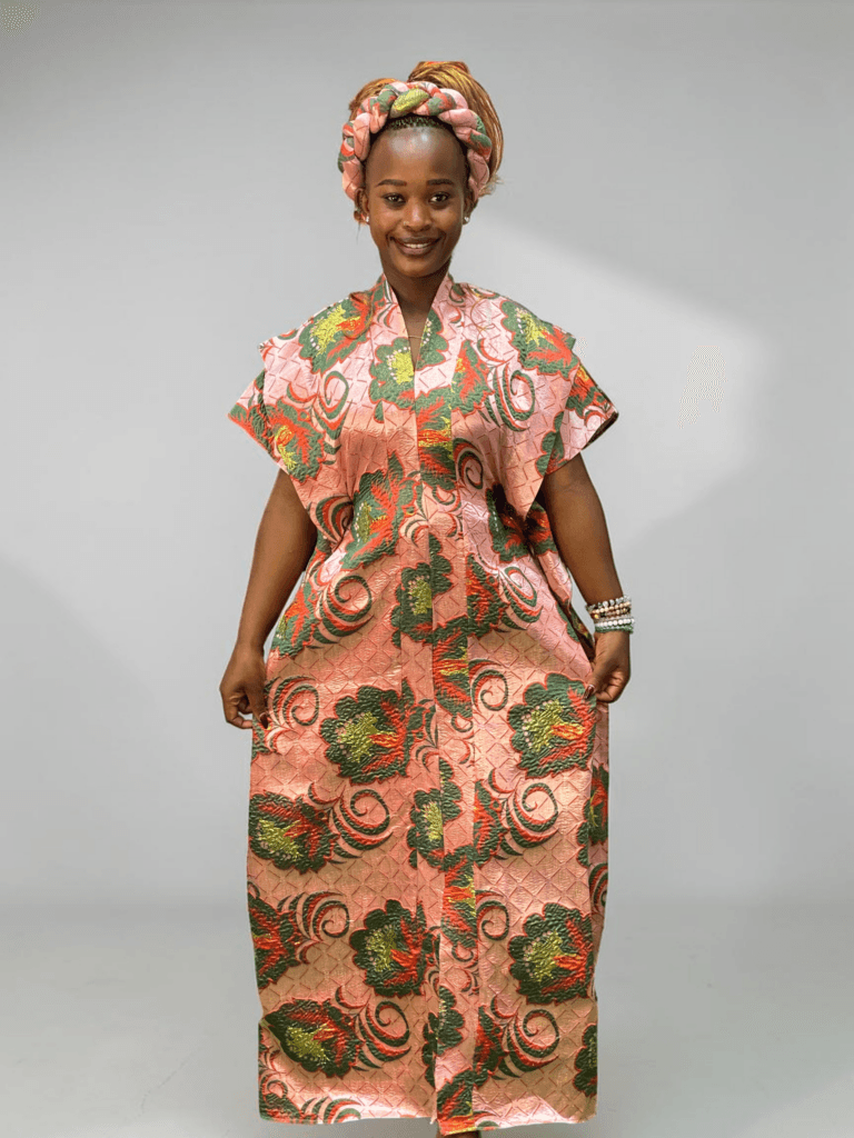 Coral pink and green floral brocade gown with woven textured pattern and adjustable waist ties on grey studio background