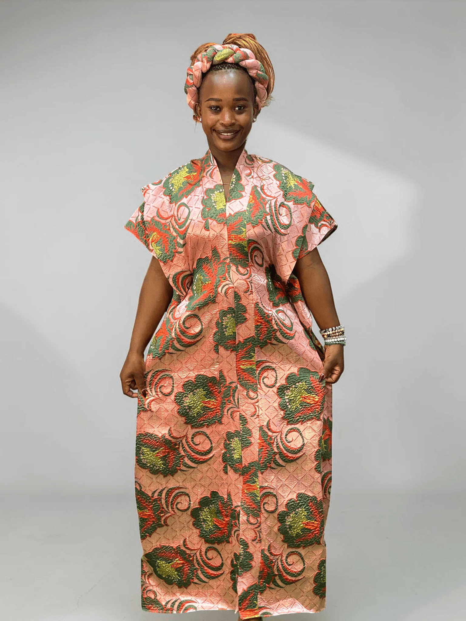 Coral pink and green floral brocade gown with woven textured pattern and adjustable waist ties on grey studio background