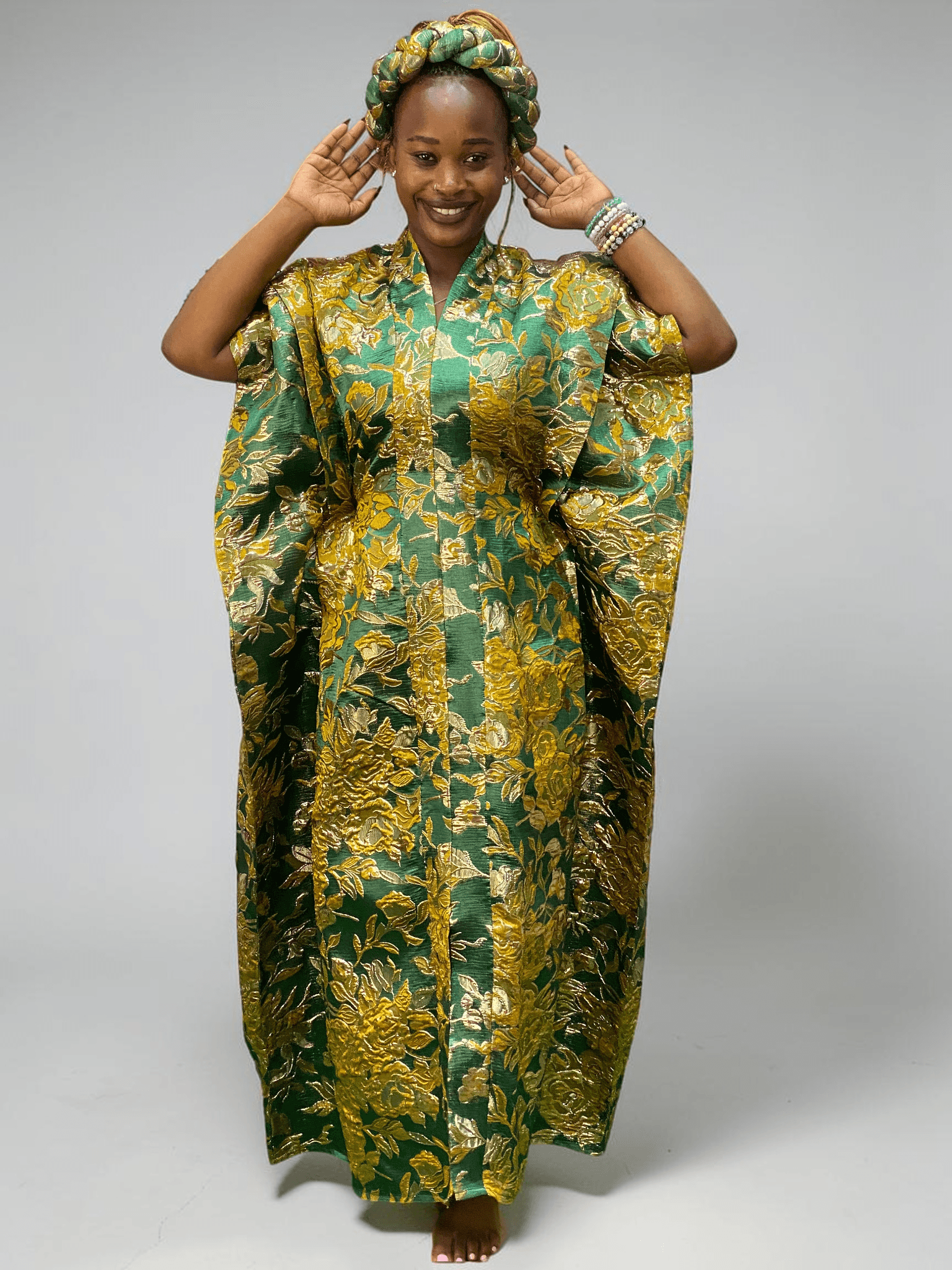 Emerald green and gold floral brocade gown with woven textured pattern and adjustable waist ties on grey studio background