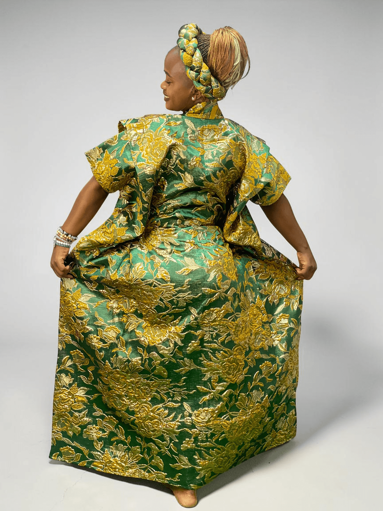 Emerald green and gold floral brocade gown with woven textured pattern and adjustable waist ties on grey studio background