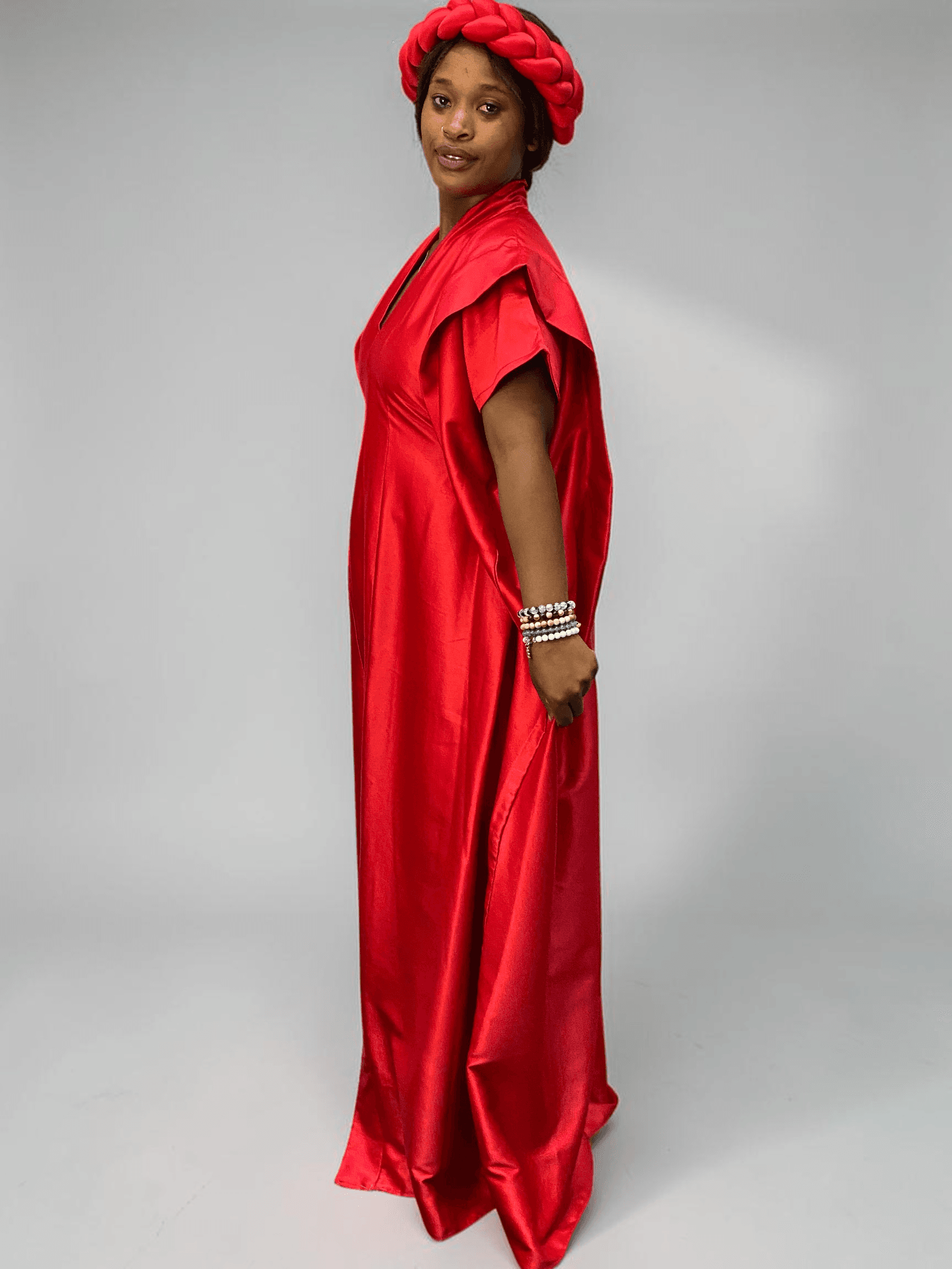 Crimson red satin boubou gown with wide sleeves and adjustable waist ties on grey studio background