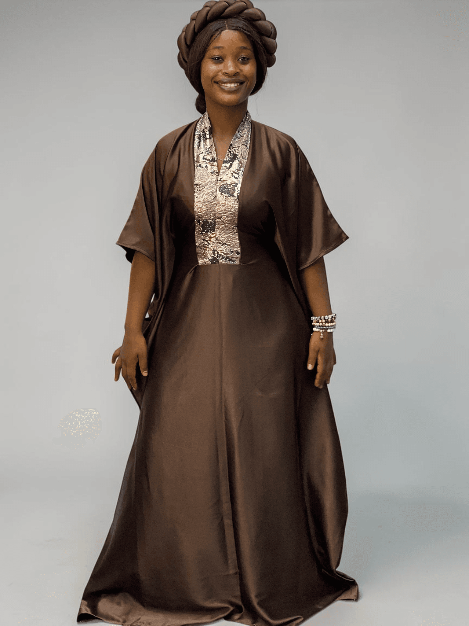 Chocolate brown satin boubou gown with brocade neckline trim and adjustable waist ties on grey studio background