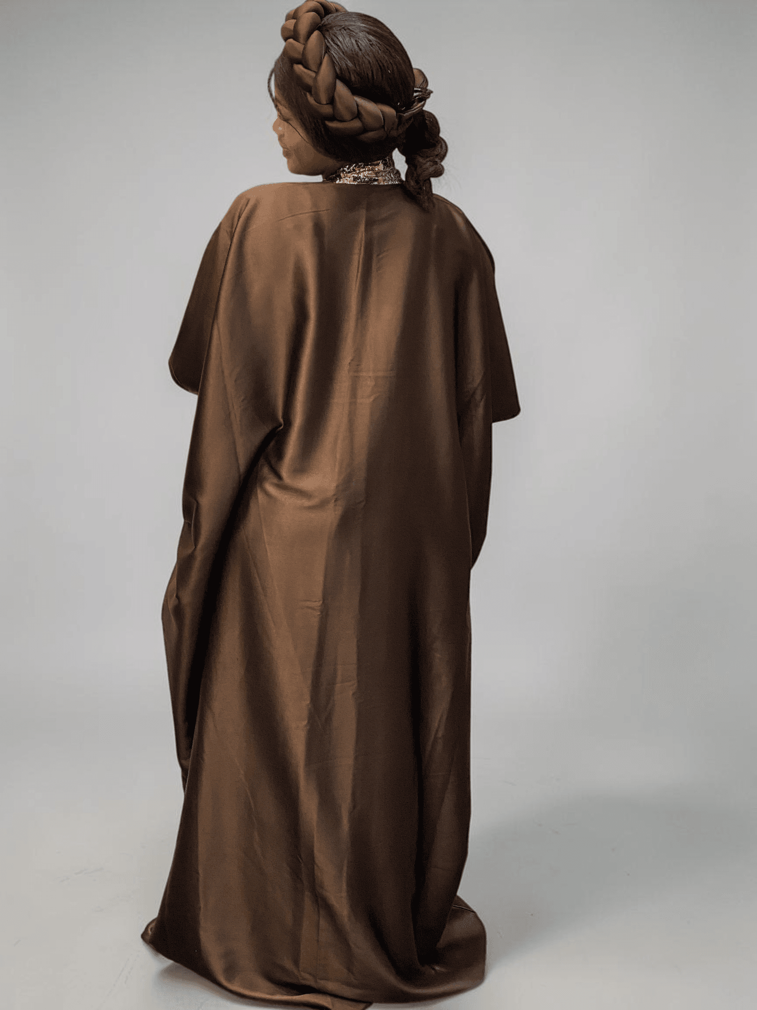 Chocolate brown satin boubou gown with brocade neckline trim and adjustable waist ties on grey studio background