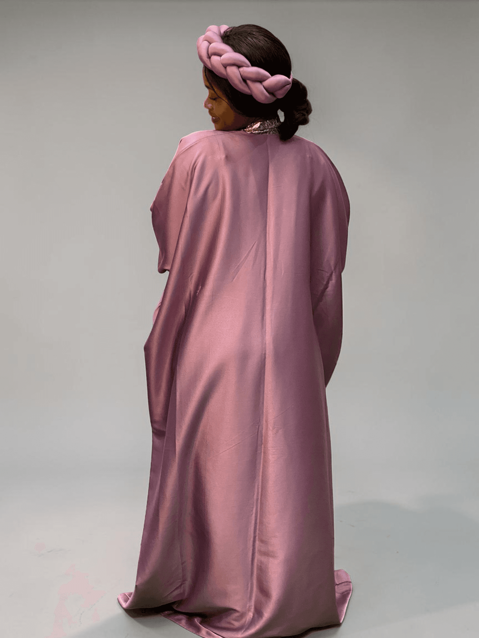 Blush pink satin boubou gown with brocade neckline trim and adjustable waist ties on grey studio background