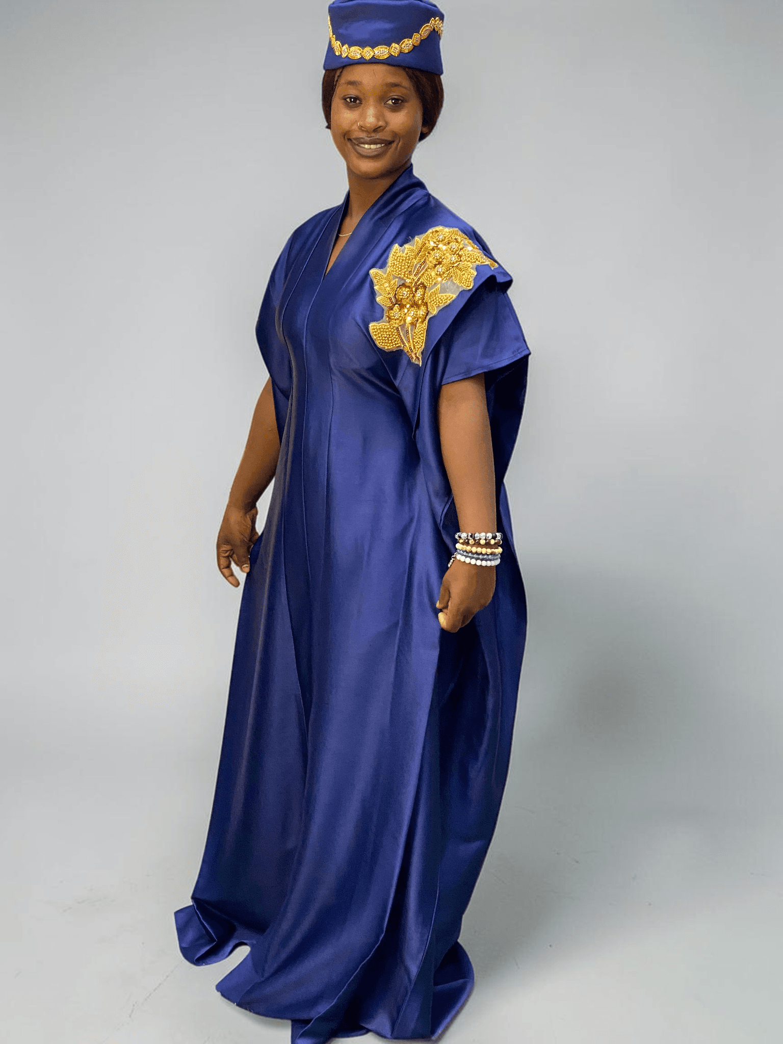 Royal blue satin boubou gown with embellished shoulder detail and adjustable waist ties on grey studio background