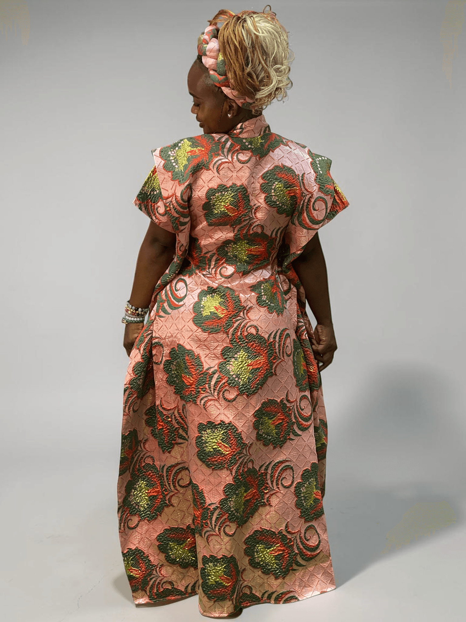Coral pink and green floral brocade gown with woven textured pattern and adjustable waist ties on grey studio background