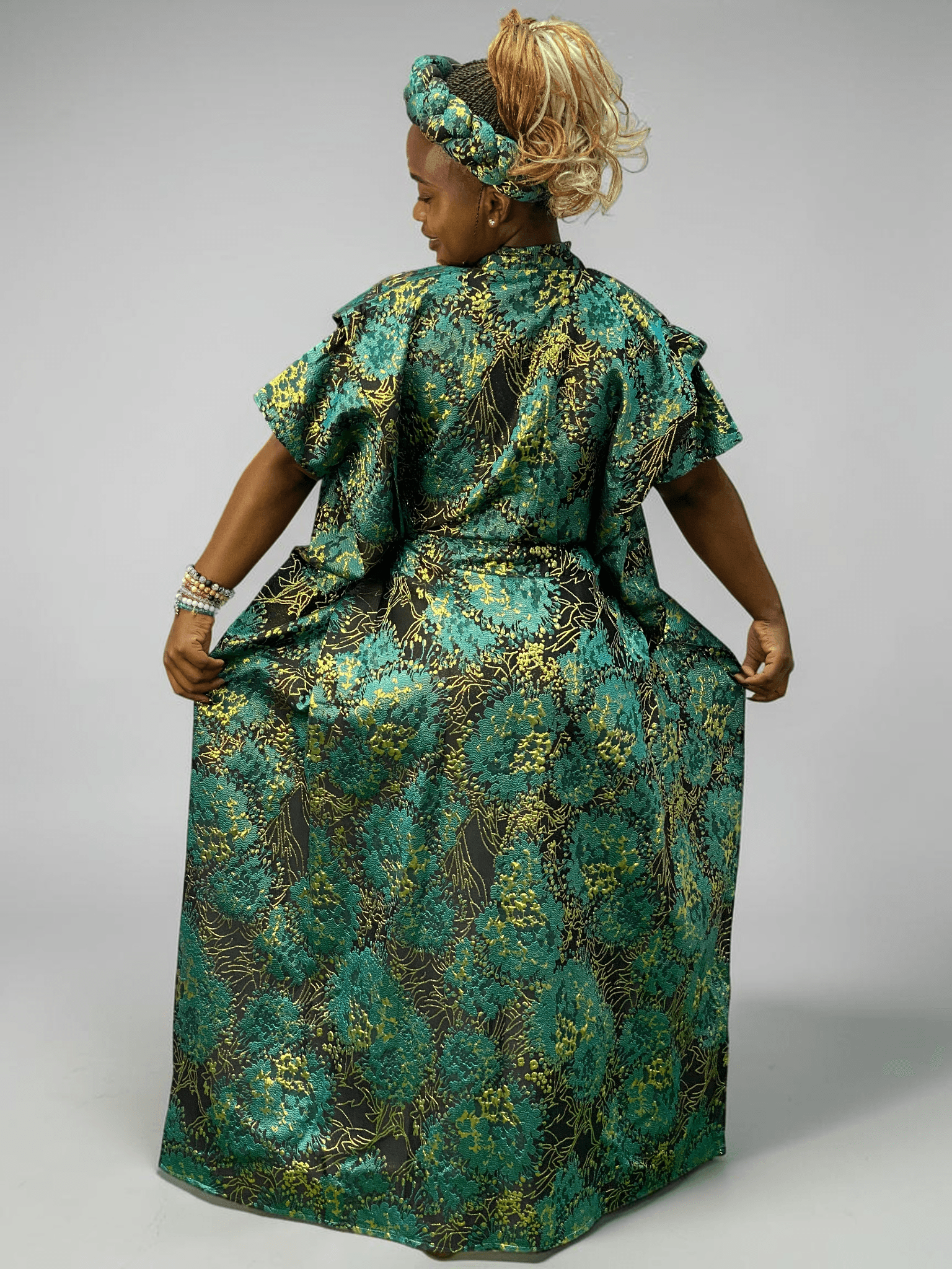 Teal green and gold floral brocade gown with woven textured pattern and adjustable waist ties on grey studio background