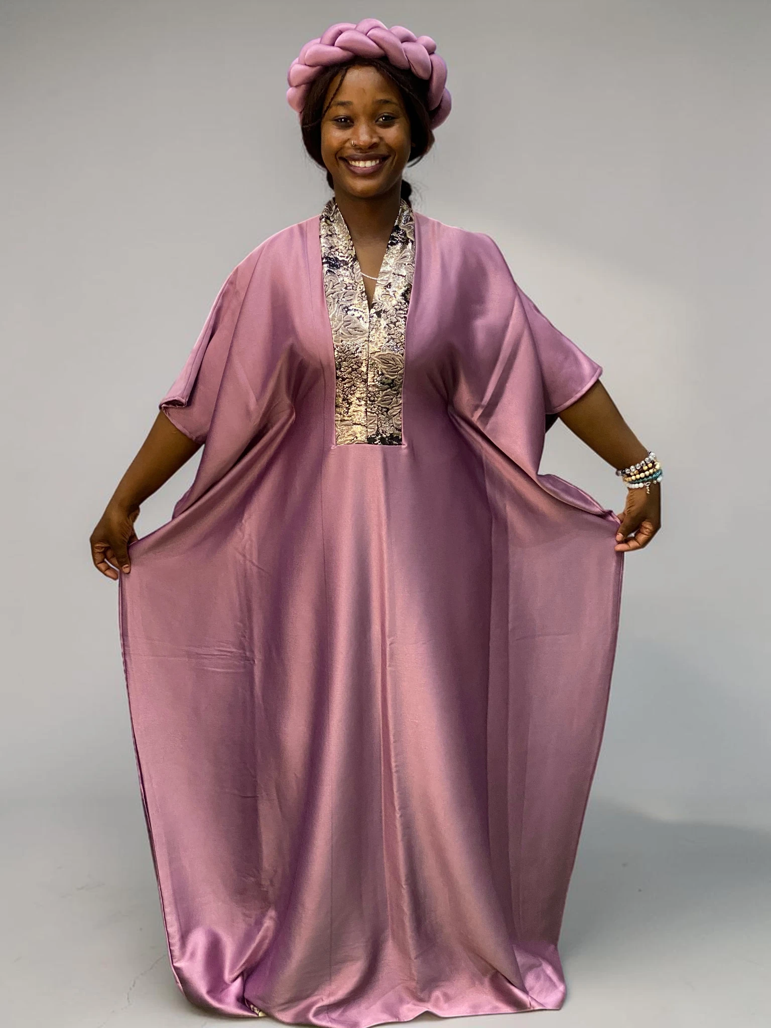 Blush pink satin boubou gown with brocade neckline trim and adjustable waist ties on grey studio background
